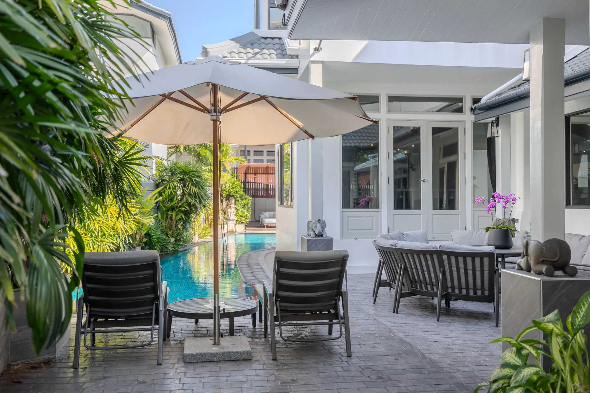 Two sun loungers under an umbrella beside the private pool, with curved sofa seating on the terrace at Villa Oasis